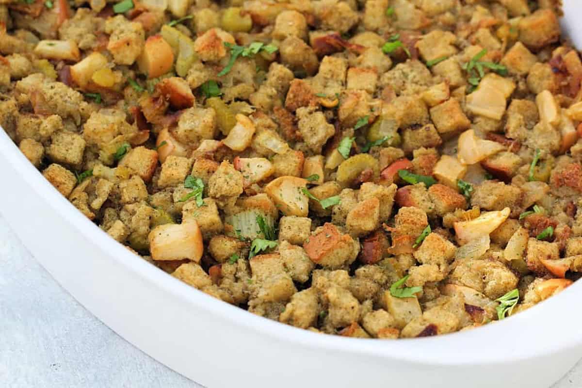 A white casserole dish filled with seasoned croutons and herbs, baked to a golden brown.