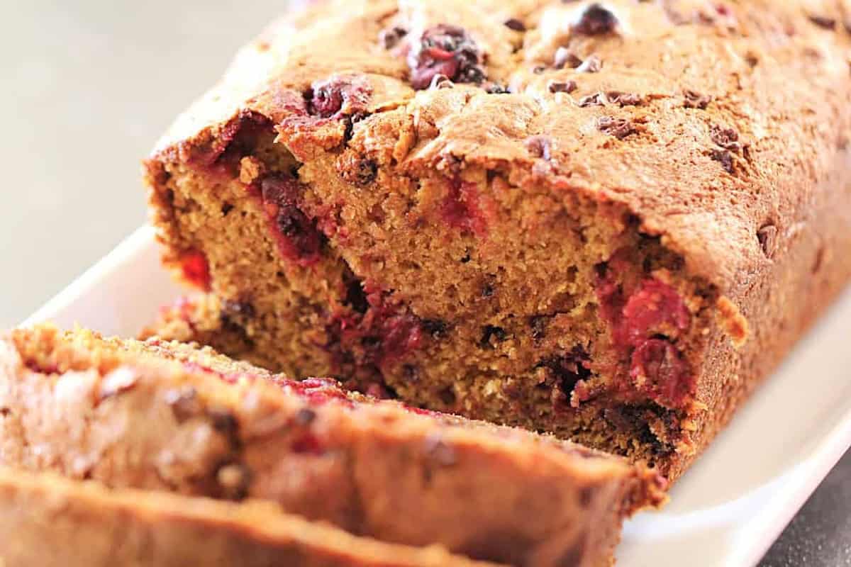 A close-up view of a sliced loaf of berry bread, showing a golden-brown crust and speckled with pieces of red berries.