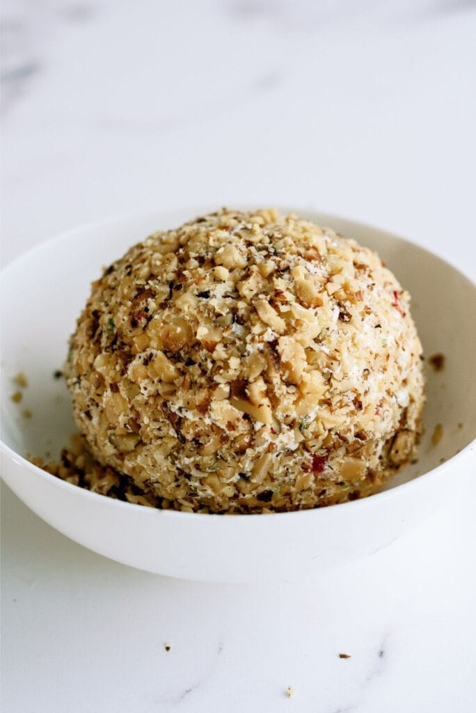 A cheese ball covered in chopped nuts on a white plate.