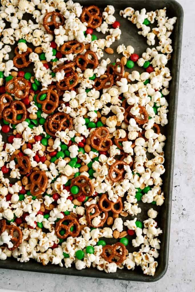 A baking sheet filled with popcorn, pretzels, and red and green candy-coated chocolates.