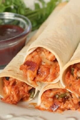 Three rolled tortillas filled with shredded chicken and melted cheese, served with a side of BBQ sauce.