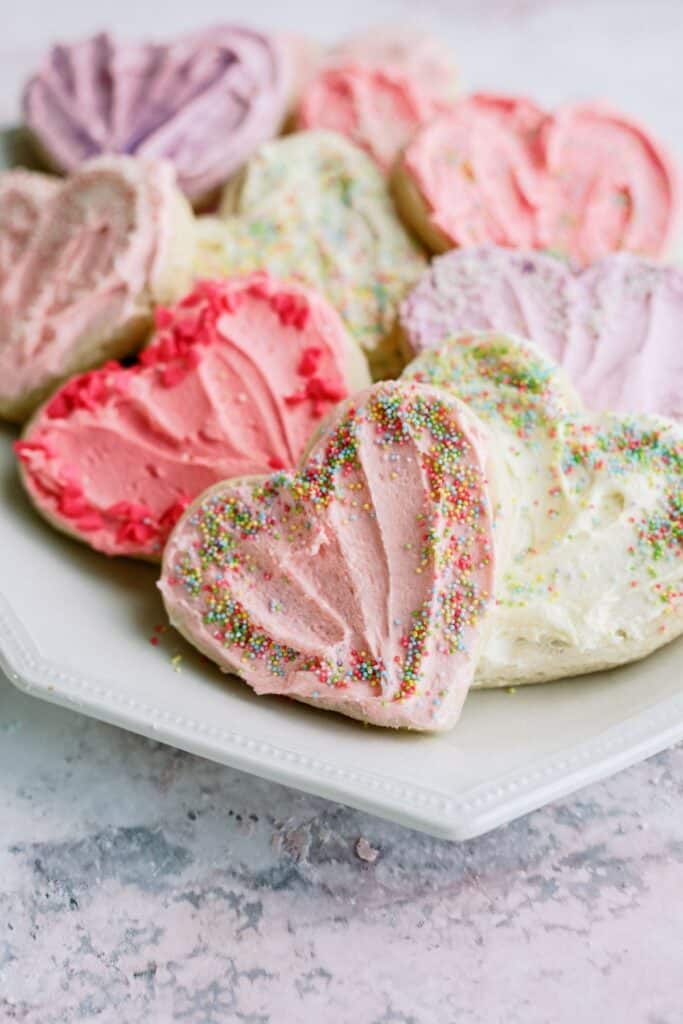 A plate of Valentine Sugar Cookies decorated with different colored frosting and sprinkles.
