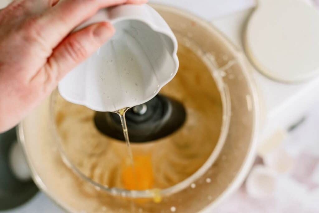 Adding an egg to sugar cookie dough mixture in a mixing bowl.