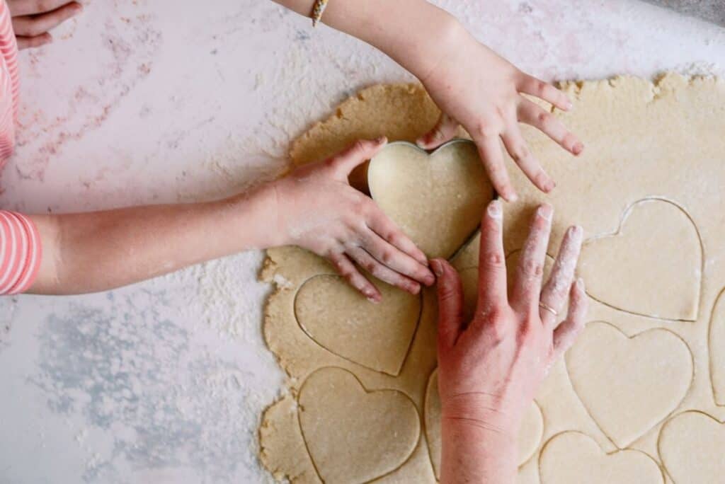 Adult and Child cutting out sugar cookie dough with a heart shaped cookie cutter.