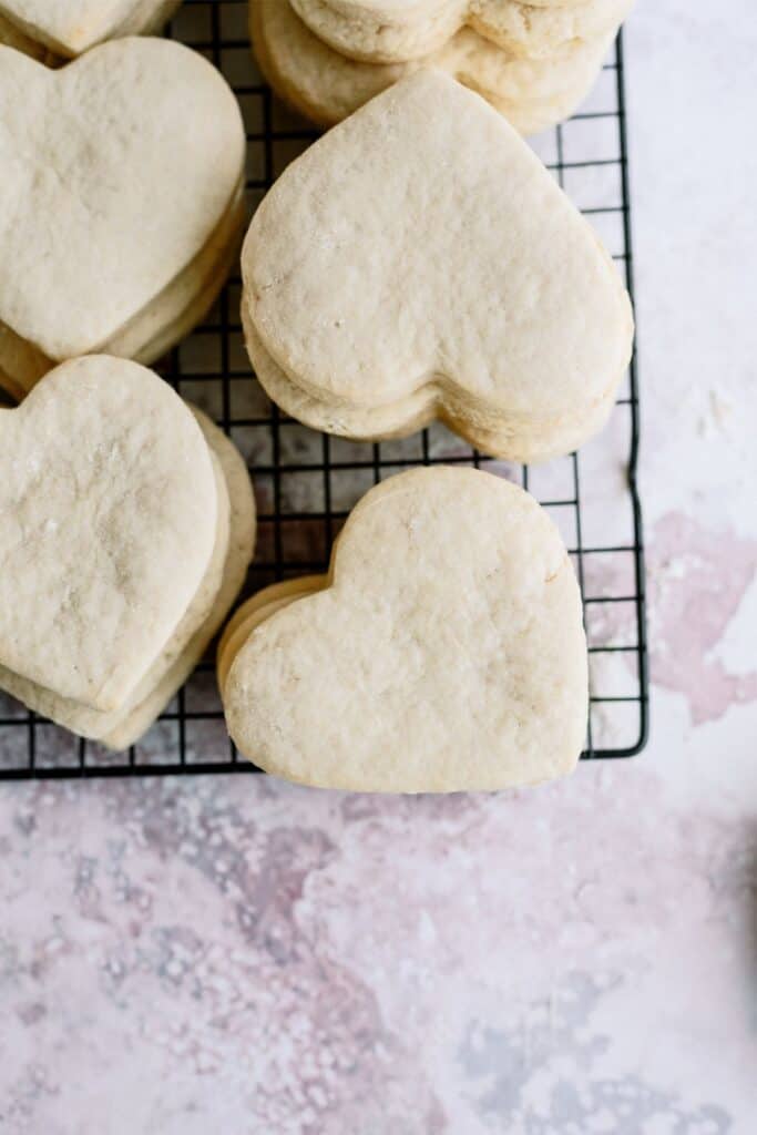 Fresh baked heart shaped sugar cookies on a cooling rack.