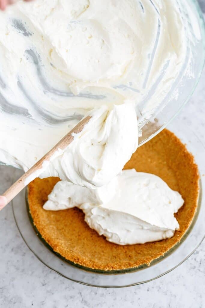 Spooning cream cheese filling into pie crust with wooden spoon.