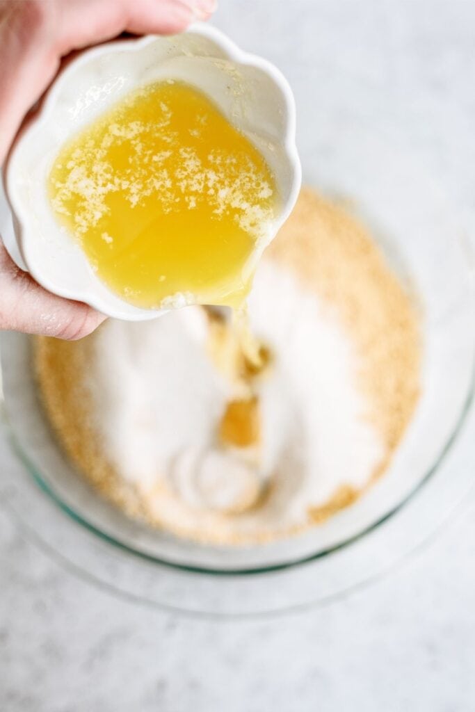 Adding melted butter to graham cracker crumb mixture in mixing bowl.