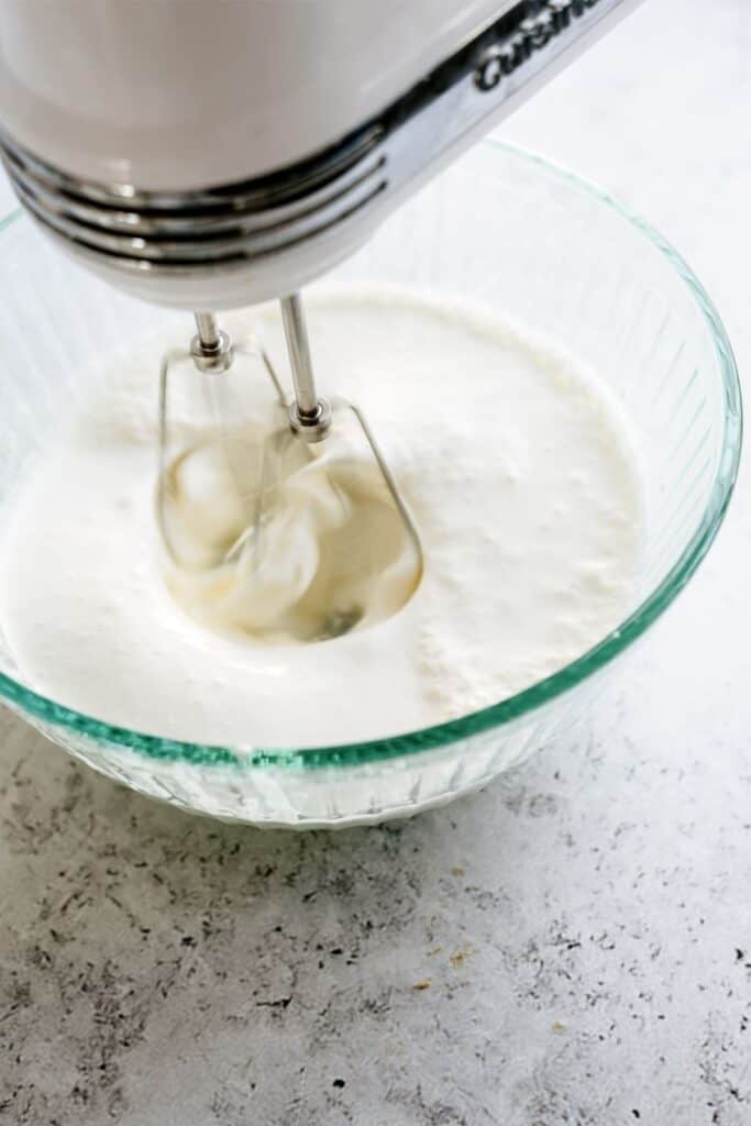 Cream cheese mixture in a glass bowl getting mixed by a hand mixer.