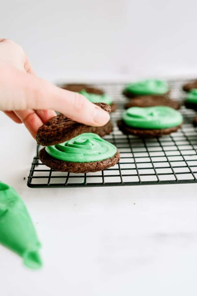 Putting a chocolate cookie on top of another frosted chocolate cookie to create a Grasshopper Sandwich Cookie.