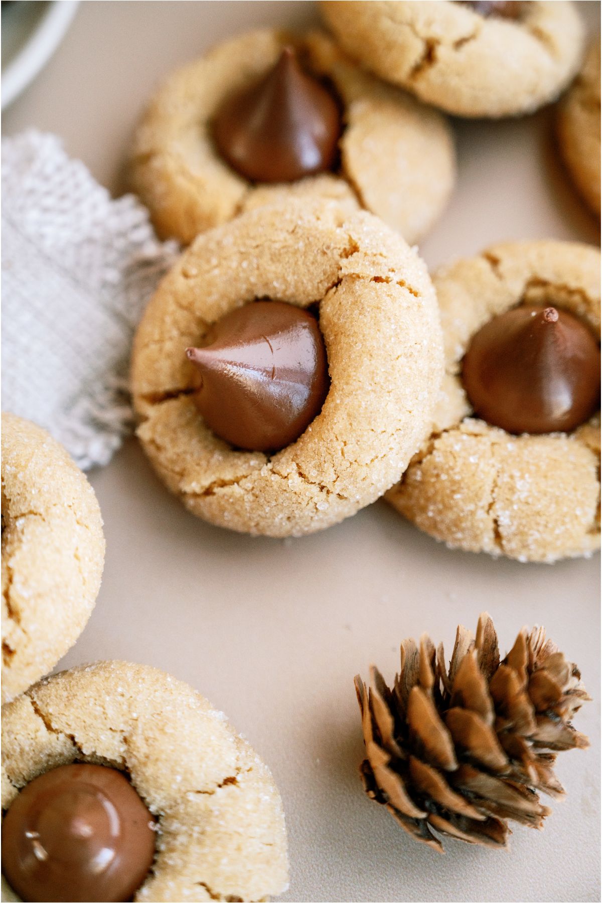 Peanut Butter Blossoms (Hershey’s Kiss Cookies) on the counter with one stacked and a small pine cone.