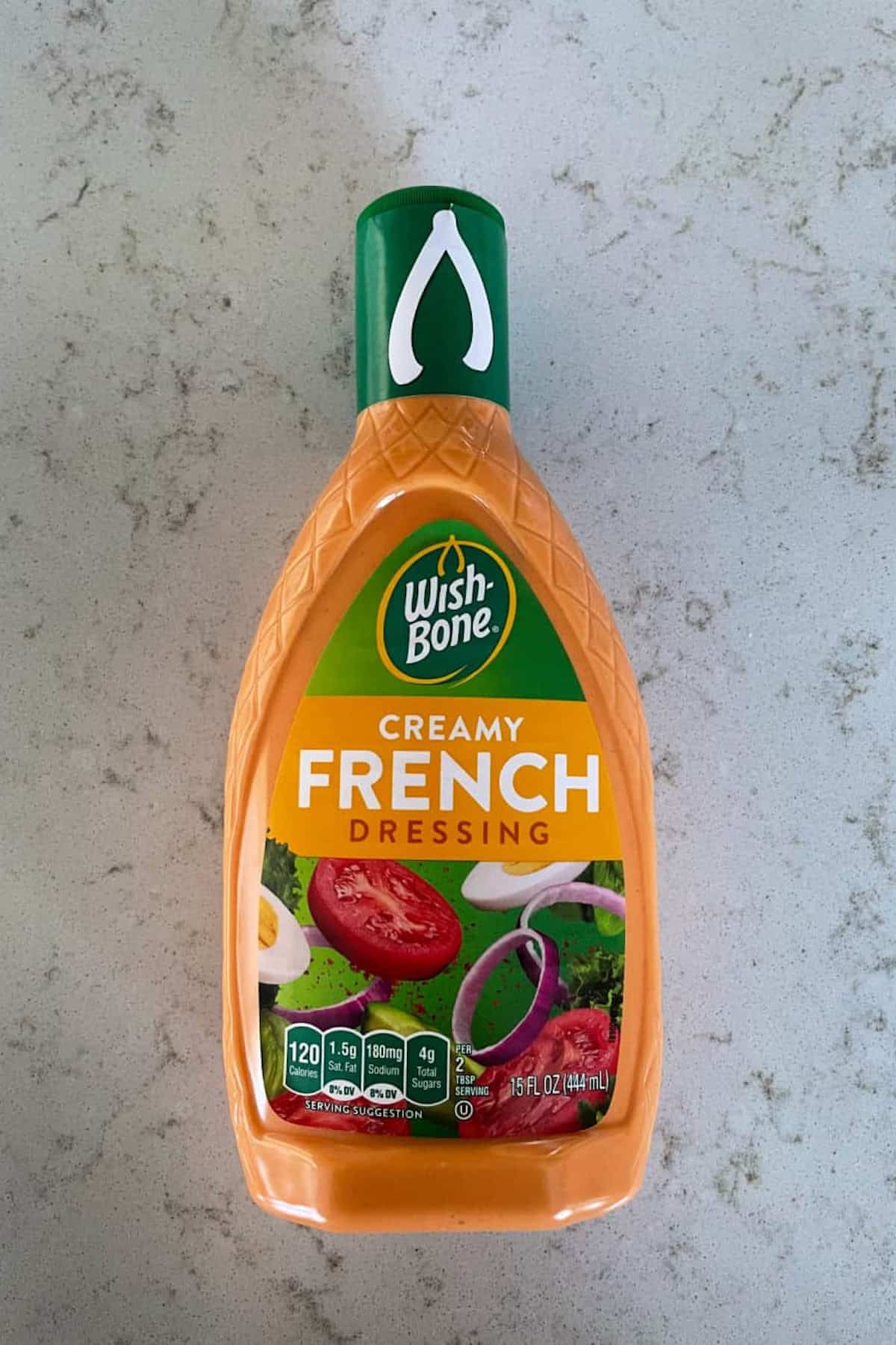 A bottle of Wish-Bone Creamy French Dressing with a green cap, placed on a light-colored marble surface. The label features images of tomatoes, onions, and lettuce.