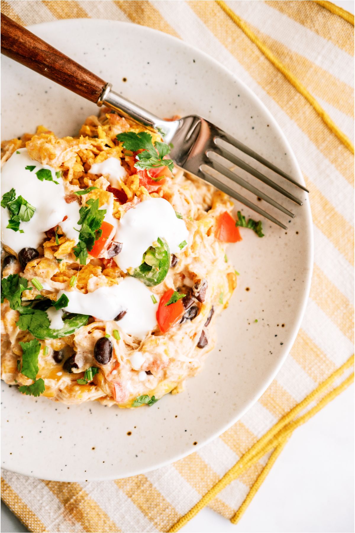 Top view of a serving of Chicken Taco Casserole on a plate topped with sour cream with a fork on the side.