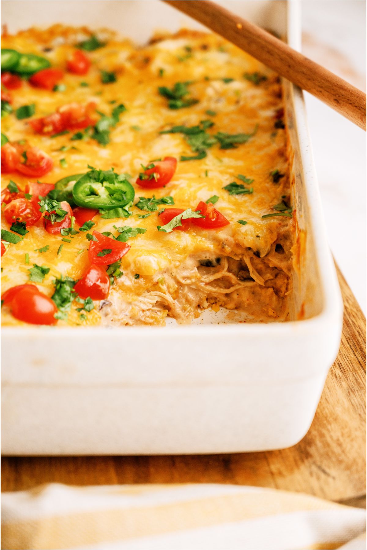 Front view of Chicken Taco Casserole in casserole dish with a wooden spoon resting on top and a square of casserole missing from the dish to show the insde of the casserole.