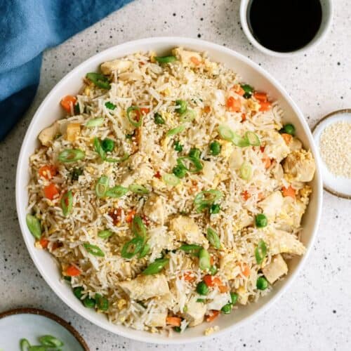 A white bowl filled with chicken fried rice with small cups of soy sauce and green onions on the side.