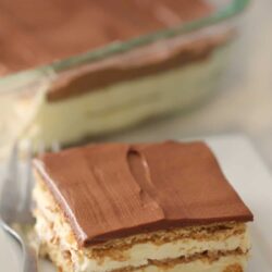 A slice of No Bake Eclair Cake on a plate with the rest of the cake in the background