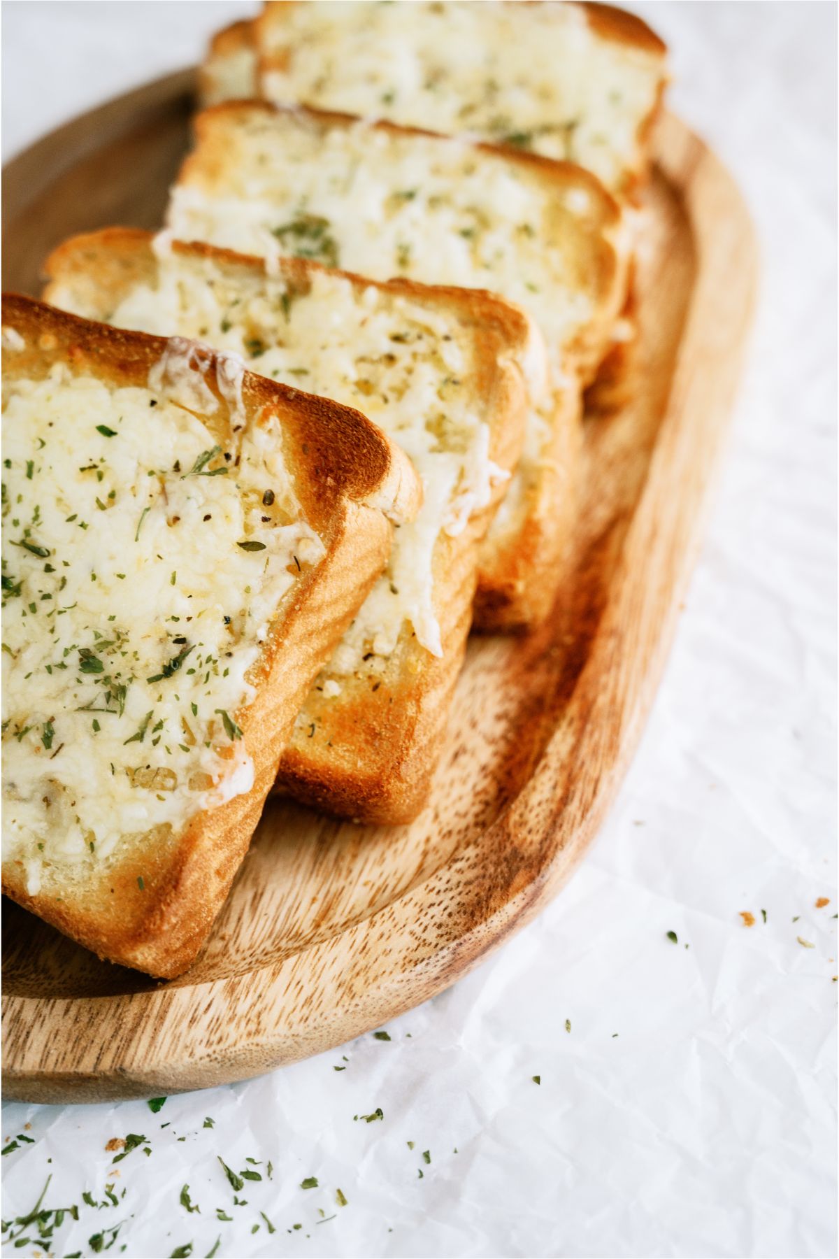 Slices of garlic bread topped with melted cheese and herbs on a wooden platter.