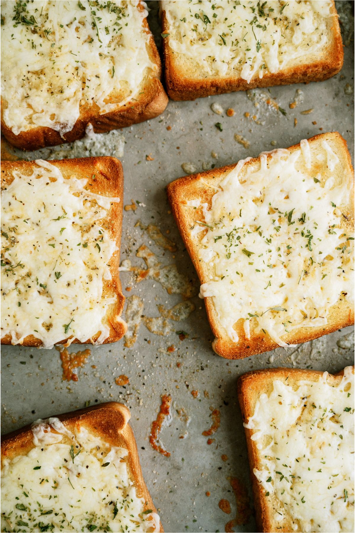 Toasted bread slices topped with melted cheese and herbs on a baking tray.