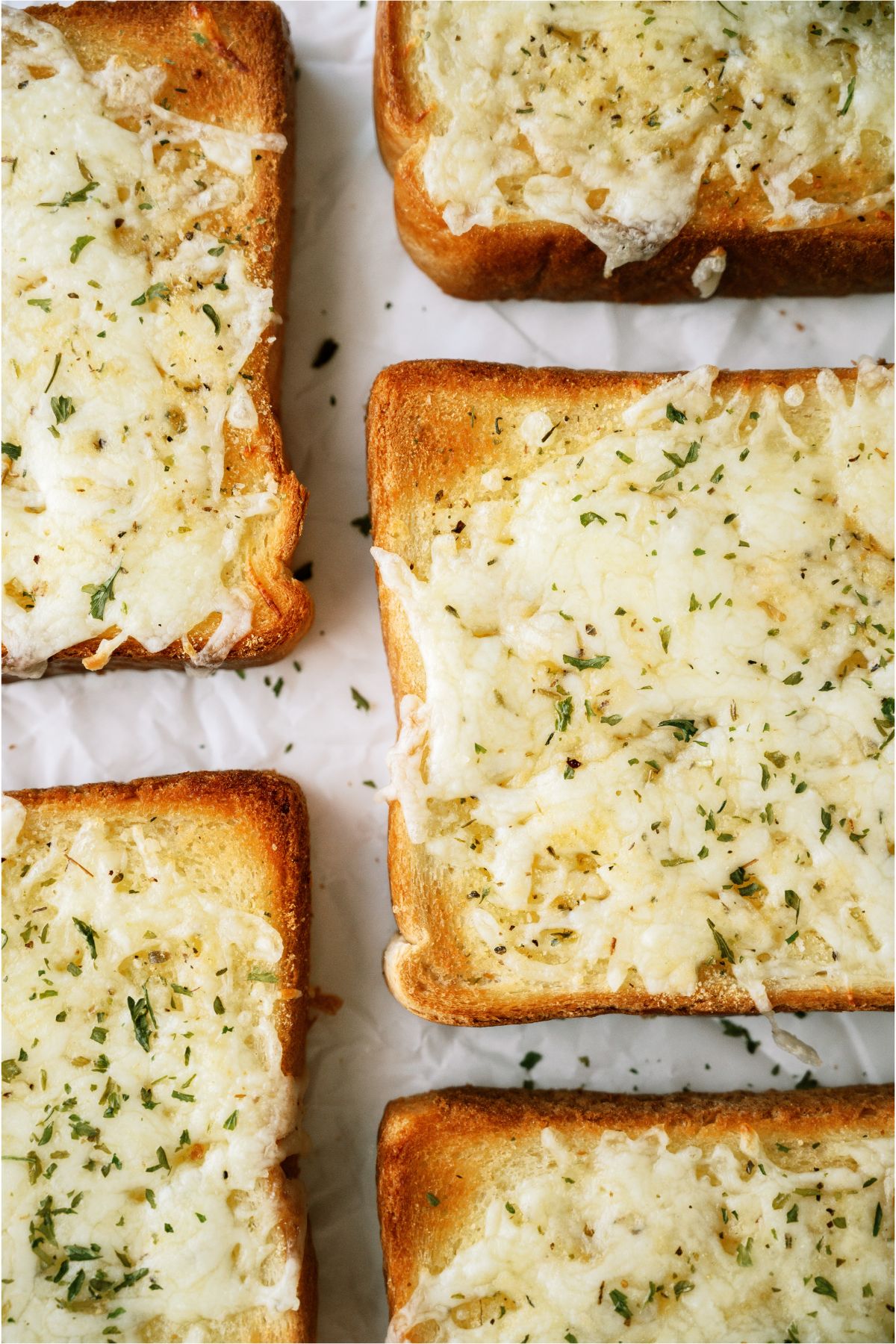 Slices of garlic bread topped with melted cheese and sprinkled with herbs on a white surface.