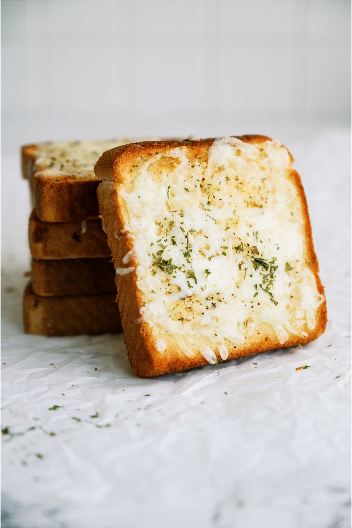 Toast slices topped with melted cheese and herbs are stacked on a white surface.