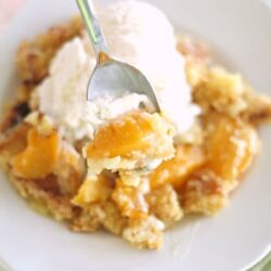 A slice of Peach Cobbler Dump Cake (4 Ingredients) on a plate topped with ice cream