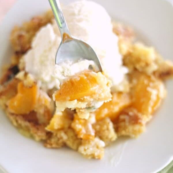 A slice of Peach Cobbler Dump Cake (4 Ingredients) on a plate topped with ice cream