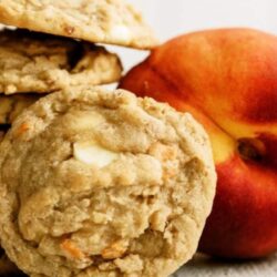 A stack of cookies is placed next to a whole peach on a white surface.