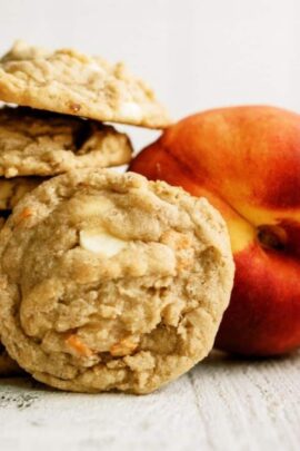 A stack of cookies is placed next to a whole peach on a white surface.