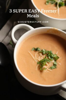 A bowl of creamy tomato soup garnished with shredded cheese and chopped herbs.