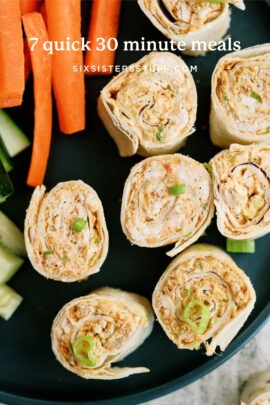 Close-up of tortilla pinwheels filled with a creamy mixture, garnished with green onions, served on a plate with carrot and cucumber sticks.