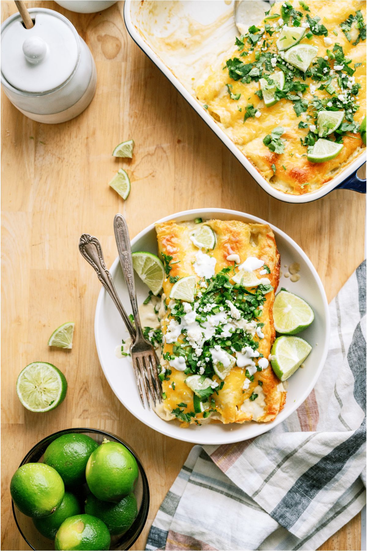 Top view of a plate of two Honey Lime Chicken Enchiladas with the pan of remaining enchiladas off to the side.