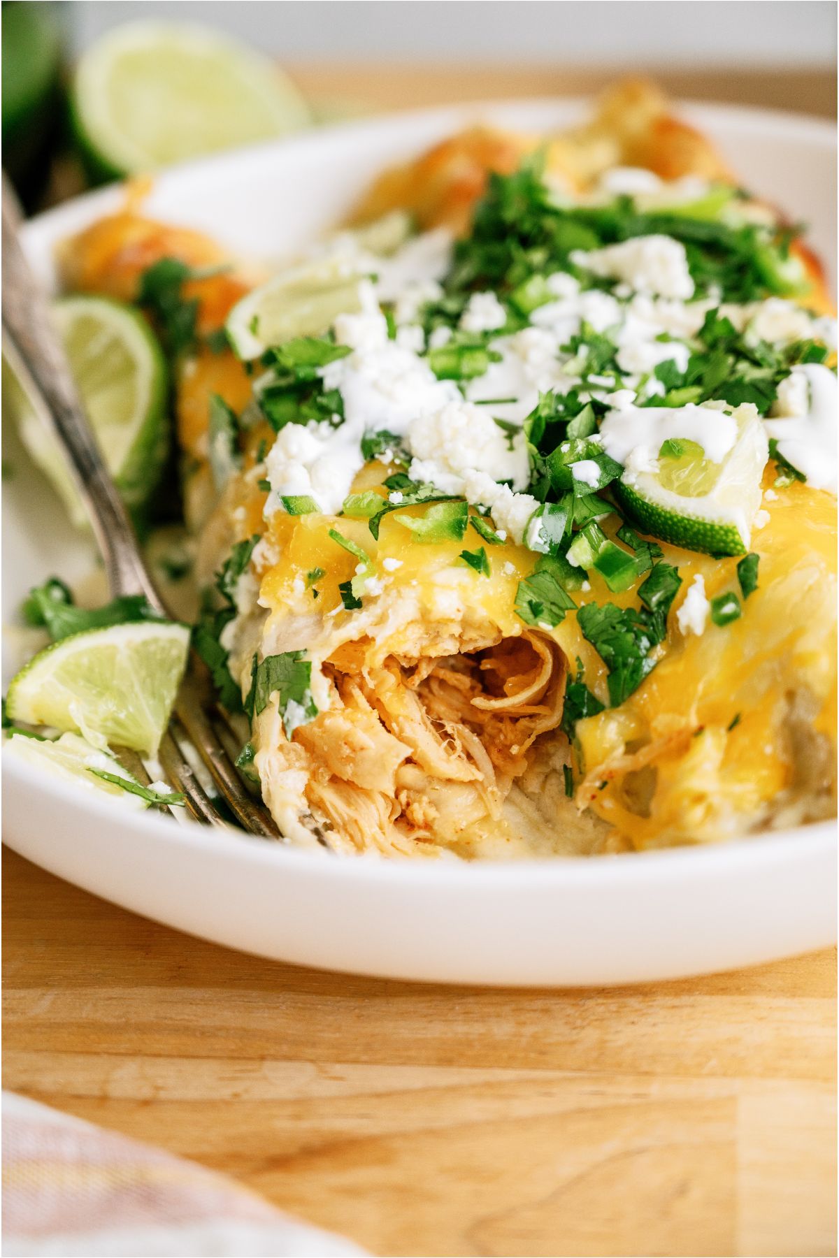 Two Honey Lime Chicken Enchiladas on a plate with toppings, one enchilada showing the shredded chicken on the inside.