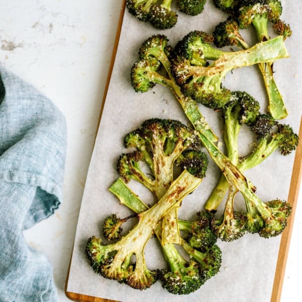 Roasted broccoli slices on a parchment-lined wooden board, with a gray cloth napkin to the left.