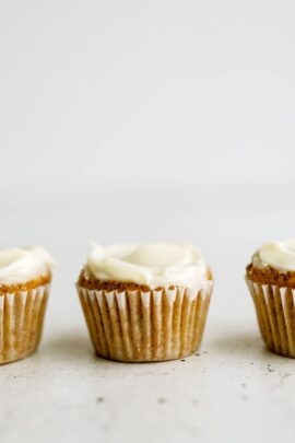 Three frosted muffins in white liners are evenly spaced in a row against a plain white background.