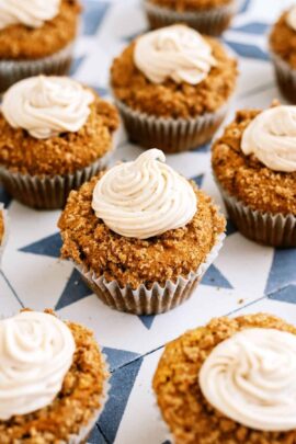 A group of pumpkin cupcakes with crumb topping and swirled frosting arranged on a patterned surface.