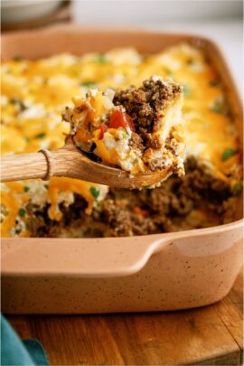 John Wayne Casserole in a casserole dish with a wooden spoon lifting out a scoop.