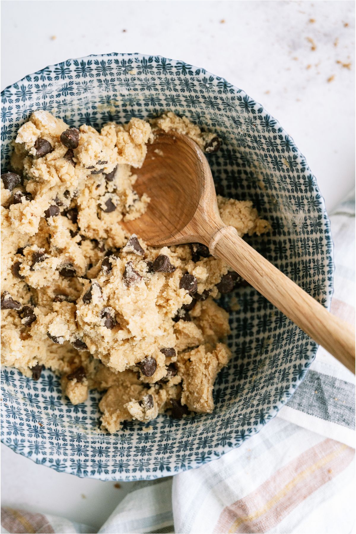 Folding chocolate chips into the cookie batter with a wooden spoon in a mixing bowl.