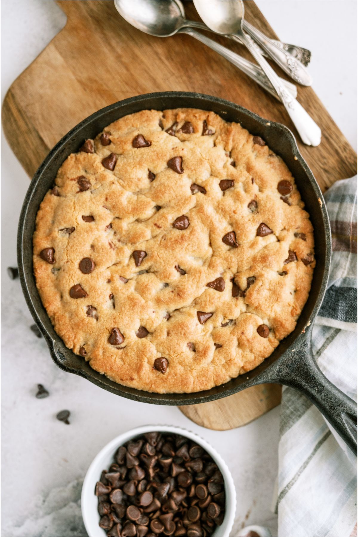 Fresh baked Pizookie in a skillet with a small bowl of chocolate chips and spoons off to the side.