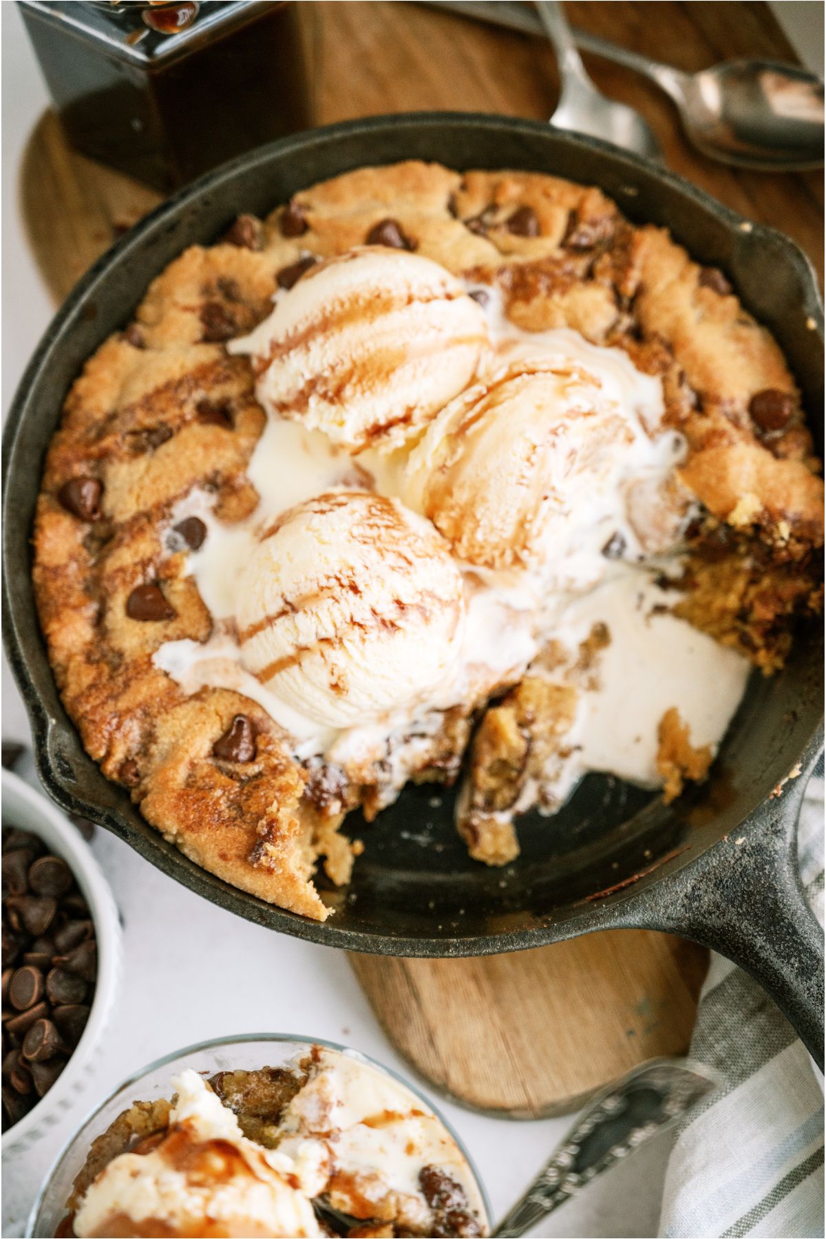 Pizookie in a skillet topped with ice cream and chocolate sauce with some bites missing.