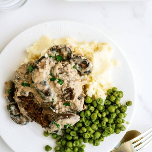 A plate of mashed potatoes, peas, and a creamy mushroom dish. A fork and knife are beside the plate.