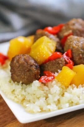 A white plate with cauliflower rice topped with meatballs, pineapple chunks, and red bell pepper pieces.