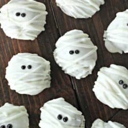 Cookies decorated to resemble mummies with white icing and black eyes, arranged on a wooden surface.