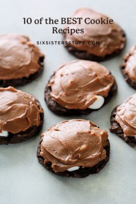 Six chocolate cookies with chocolate frosting are displayed on a light-colored surface.