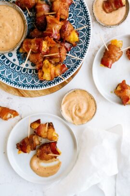 Plates of bacon-wrapped tater tots on skewers, served with dipping sauce in small bowls.