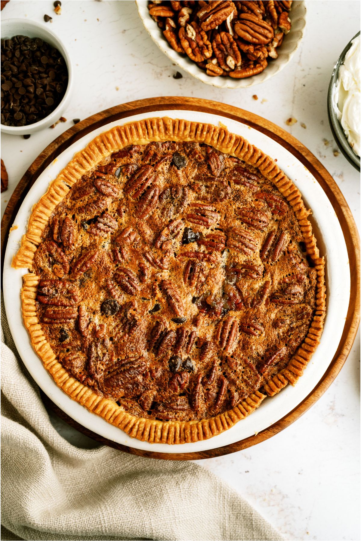 Top view of a Chocolate Pecan Pie with small bowls of pecans and chocolate on the side.