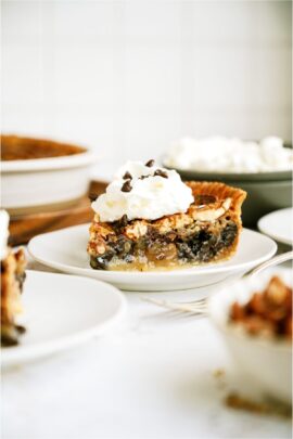 A slice of Chocolate Pecan Pie topped with whip cream on a white plate.