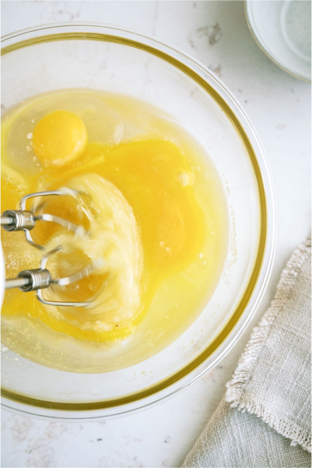 A glass bowl filled with eggs and sugar with an electric mixer beating the ingredient together.