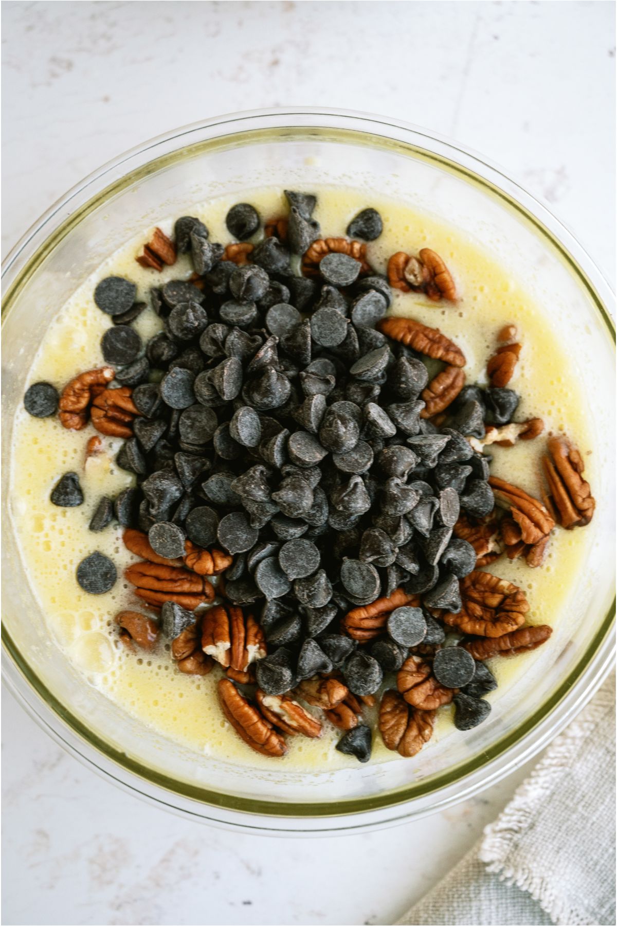 Pecans and chocolate chips added to egg mixture in glass mixing bowl.