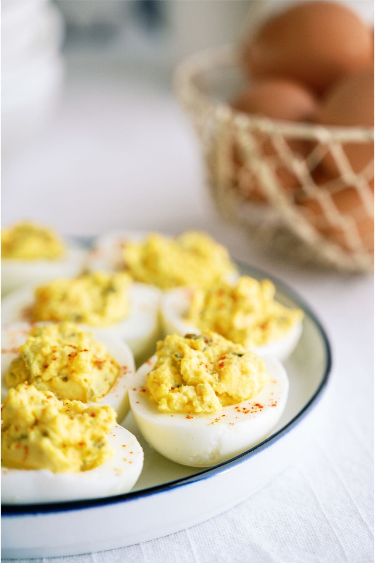 Side view of Deviled Eggs on a serving plate with a basket of eggs in the background.