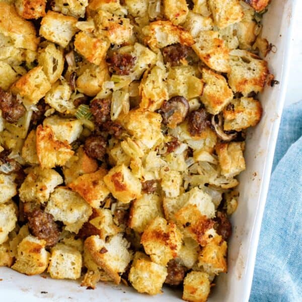 A close-up of baked stuffing with toasted bread cubes, sausage, and herbs in a white baking dish.