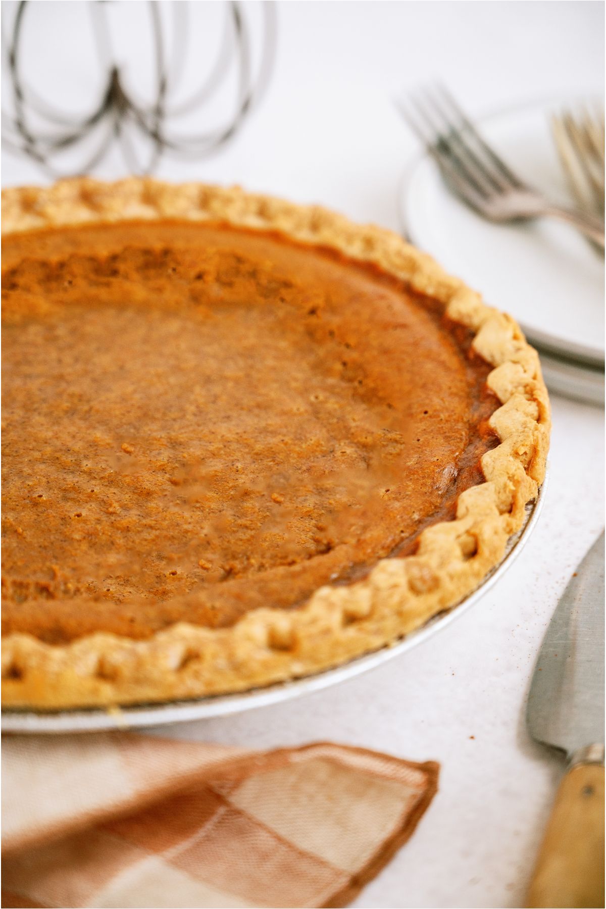 An Easy Pumpkin Pie on a counter with plates and decor in the background. A checkered towel next to the baked pie.